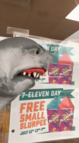 A Shark Is Standing In Front Of A Sign That Says 7 Eleven Day Free Small Slurpee GIF