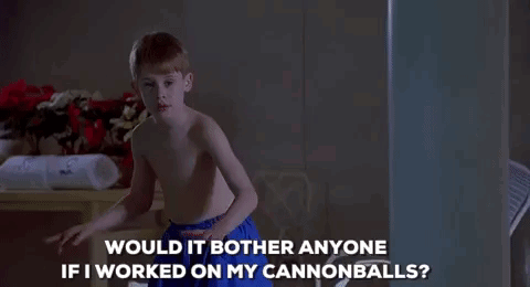 A Shirtless Boy In Blue Shorts Is Standing In A Dark Room And Talking To Someone . GIF