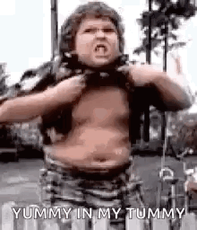 A Shirtless Boy With A Big Belly Is Standing On A Street And Yummy In My Tummy . GIF