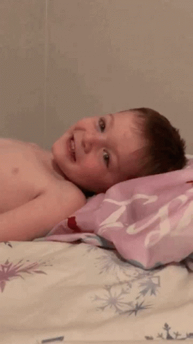 A Shirtless Child Is Laying On A Bed With A Pink Pillow That Says ' Princess ' On It GIF