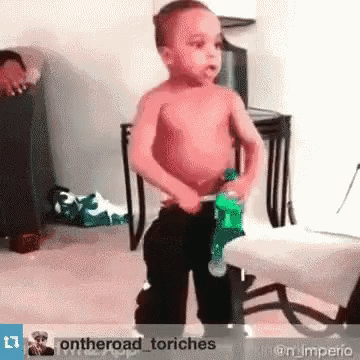 A Shirtless Little Boy Is Holding A Green Bottle In His Hand GIF