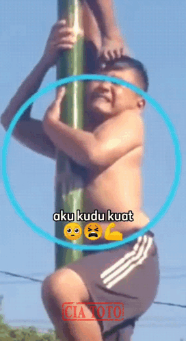 A Shirtless Man Climbs A Pole With The Words Aku Kudu Kuat On The Bottom GIF