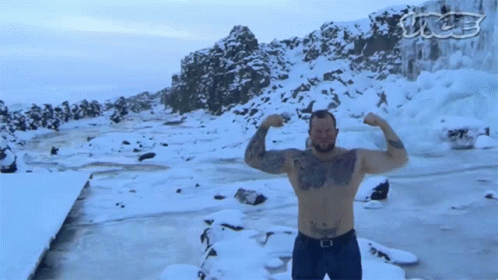 A Shirtless Man Flexes His Muscles In Front Of A Snowy Landscape GIF