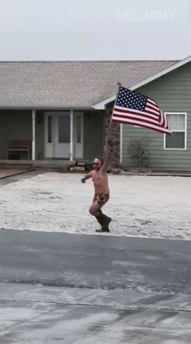 A Shirtless Man Holding An American Flag In Front Of A House GIF
