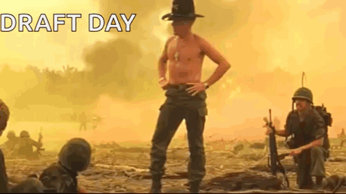 A Shirtless Man In A Cowboy Hat Is Standing In A Field With Soldiers In The Background . GIF
