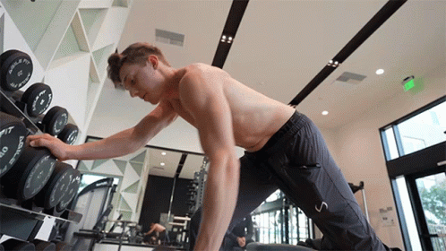 A Shirtless Man In A Gym Reaches For A Dumbbell That Says O'neill On It GIF