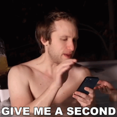 A Shirtless Man In A Hot Tub Looking At A Cell Phone With The Words Give Me A Second Below Him GIF