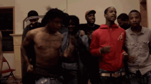 A Shirtless Man In A Red Jacket Is Surrounded By A Group Of Men GIF