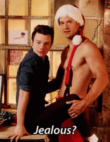 A Shirtless Man In A Santa Hat Is Sitting On A Man 'S Lap . GIF