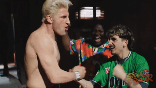 A Shirtless Man In A Street Fighter Shirt Holds Hands With Another Shirtless Man GIF