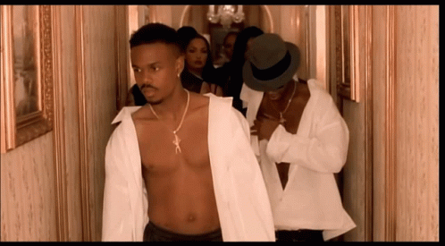 A Shirtless Man In A White Shirt Is Walking Down A Hallway With Other Men GIF