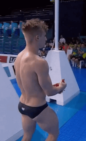 A Shirtless Man In Black Swim Trunks Stands On A Diving Board GIF