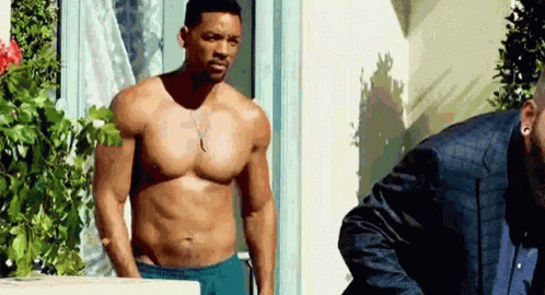 A Shirtless Man In Blue Shorts Is Standing Next To Another Man In A Suit . GIF
