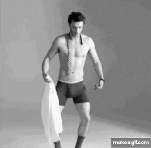 A Shirtless Man In Boxer Shorts And A Tie Is Holding A White Shirt In His Hand . GIF