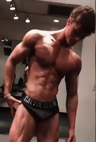 A Shirtless Man In Calvin Klein Underwear Is Standing In Front Of A Mirror In A Gym . GIF