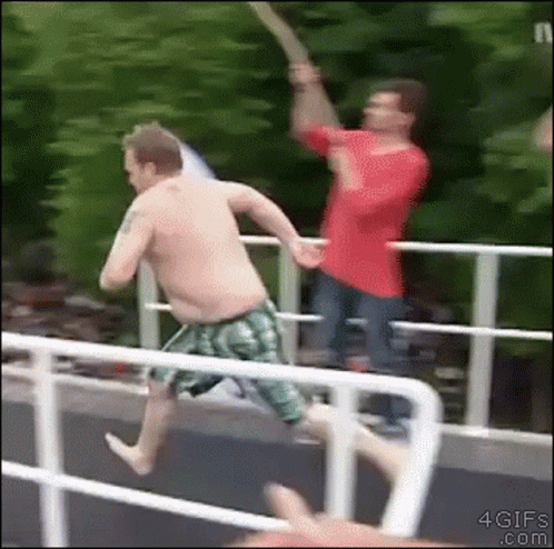a shirtless man in green shorts is jumping off a bridge
