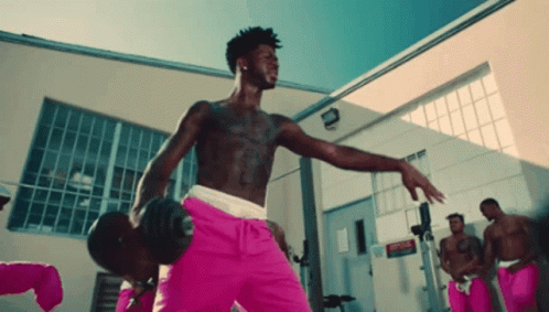 A Shirtless Man In Pink Shorts Is Holding A Dumbbell In A Gym GIF
