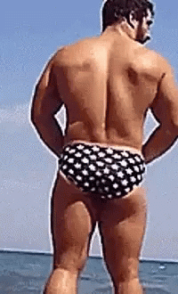 A Shirtless Man In Polka Dot Swim Trunks Is Standing In The Water . GIF