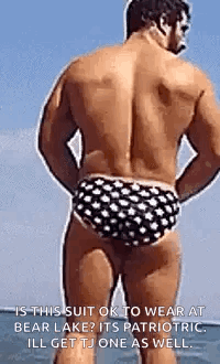 A Shirtless Man In Polka Dot Swim Trunks Is Standing On The Beach . GIF