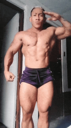 A Shirtless Man In Purple Shorts Is Giving The Peace Sign GIF