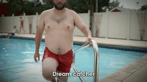 A Shirtless Man In Red Shorts Is Getting Out Of A Swimming Pool With The Words Dream Catcher Above Him GIF