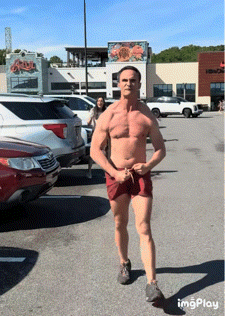 A Shirtless Man In Red Shorts Is Standing In A Parking Lot In Front Of A Building That Says King Crab GIF