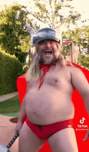 A Shirtless Man In Red Swim Trunks And A Viking Helmet Is Holding A Hammer And Smiling . GIF