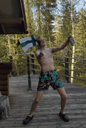 A Shirtless Man In Swim Trunks Is Holding A Flag And A Can Of Beer GIF