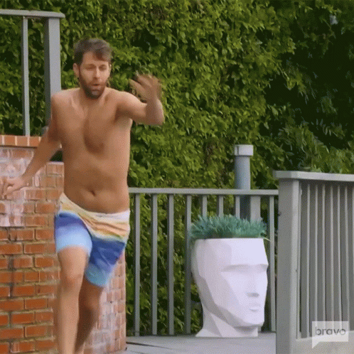 A Shirtless Man In Swim Trunks Is Running On A Deck With A Bravo Logo In The Background GIF