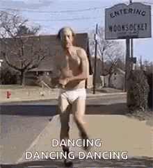 A Shirtless Man In Underwear Is Dancing On A Sidewalk In Front Of A Sign That Says Dancing Dancing . GIF