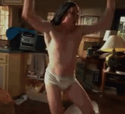 A Shirtless Man In Underwear Is Standing In A Living Room With His Arms In The Air . GIF