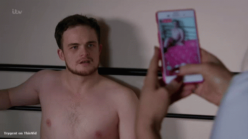 A Shirtless Man Is Being Photographed On A Cell Phone By Someone With Itv Written On The Bottom Of The Screen GIF