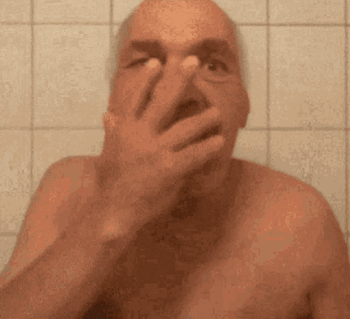 A Shirtless Man Is Covering His Face With His Hand In A Bathroom . GIF