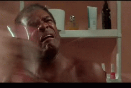 A Shirtless Man Is Crying In Front Of A Shelf With Bottles Of Perfume GIF
