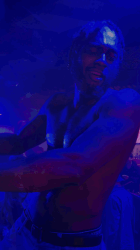 A Shirtless Man Is Dancing In A Dark Room With A Blue Light Behind Him GIF