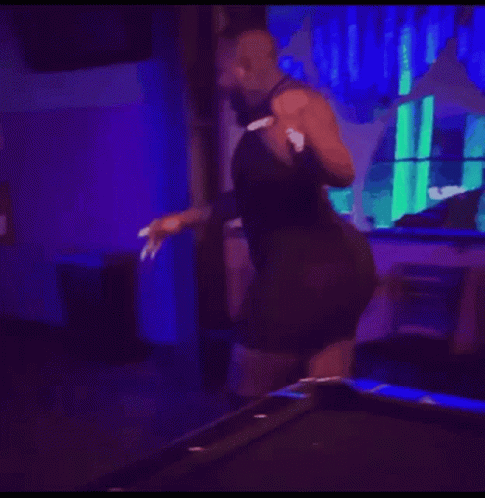 A Shirtless Man Is Dancing In A Dark Room With A Red Exit Sign . GIF