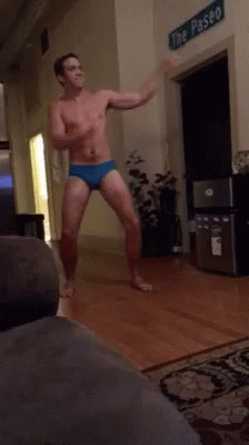 A Shirtless Man Is Dancing In A Living Room In Front Of A Sign That Says The Paseo GIF