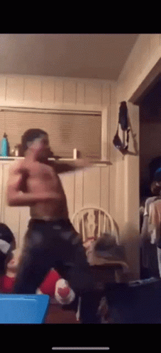 A Shirtless Man Is Dancing In A Living Room With A Chair In The Background GIF