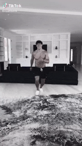 A Shirtless Man Is Dancing In A Living Room With A Couch . GIF
