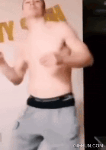 A Shirtless Man Is Dancing In A Room With A Sign That Says N On It . GIF