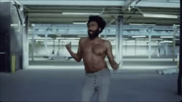 A Shirtless Man Is Dancing In An Empty Parking Garage . GIF