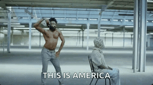 A Shirtless Man Is Dancing In An Empty Room Next To A Man In A Chair . GIF
