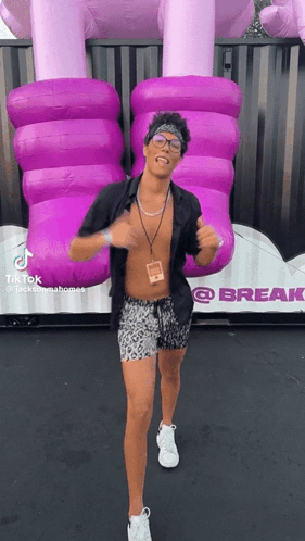 A Shirtless Man Is Dancing In Front Of A Giant Purple Inflatable Elephant GIF