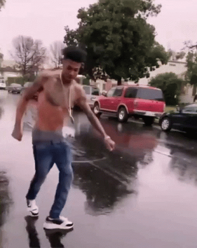 A Shirtless Man Is Dancing In The Rain On A Wet Street GIF