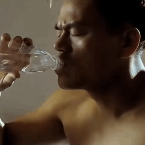 A Shirtless Man Is Drinking Water From A Bottle . GIF