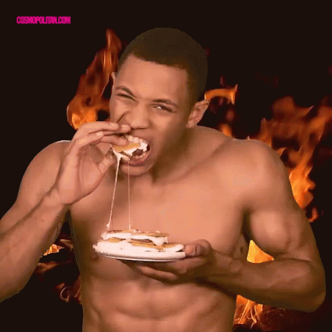A Shirtless Man Is Eating A Sandwich With Flames In The Background And The Words Cosmopolitan.com Visible GIF