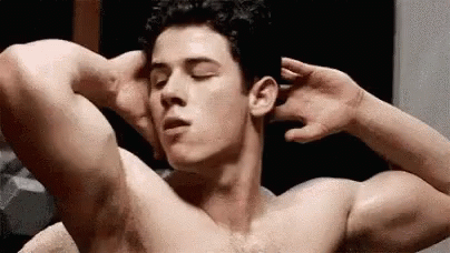 A Shirtless Man Is Flexing His Muscles In A Locker Room . GIF