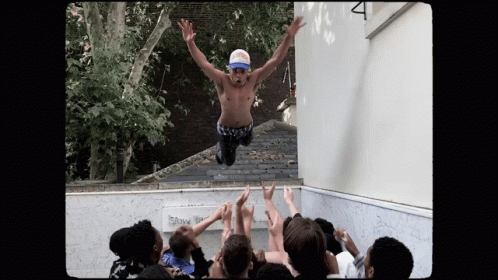 A Shirtless Man Is Jumping In The Air With His Arms Outstretched In Front Of A Crowd GIF