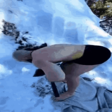 A Shirtless Man Is Kneeling Down In The Snow Holding A Hammer . GIF