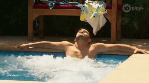 A Shirtless Man Is Laying In A Jacuzzi Pool With His Arms Outstretched . GIF